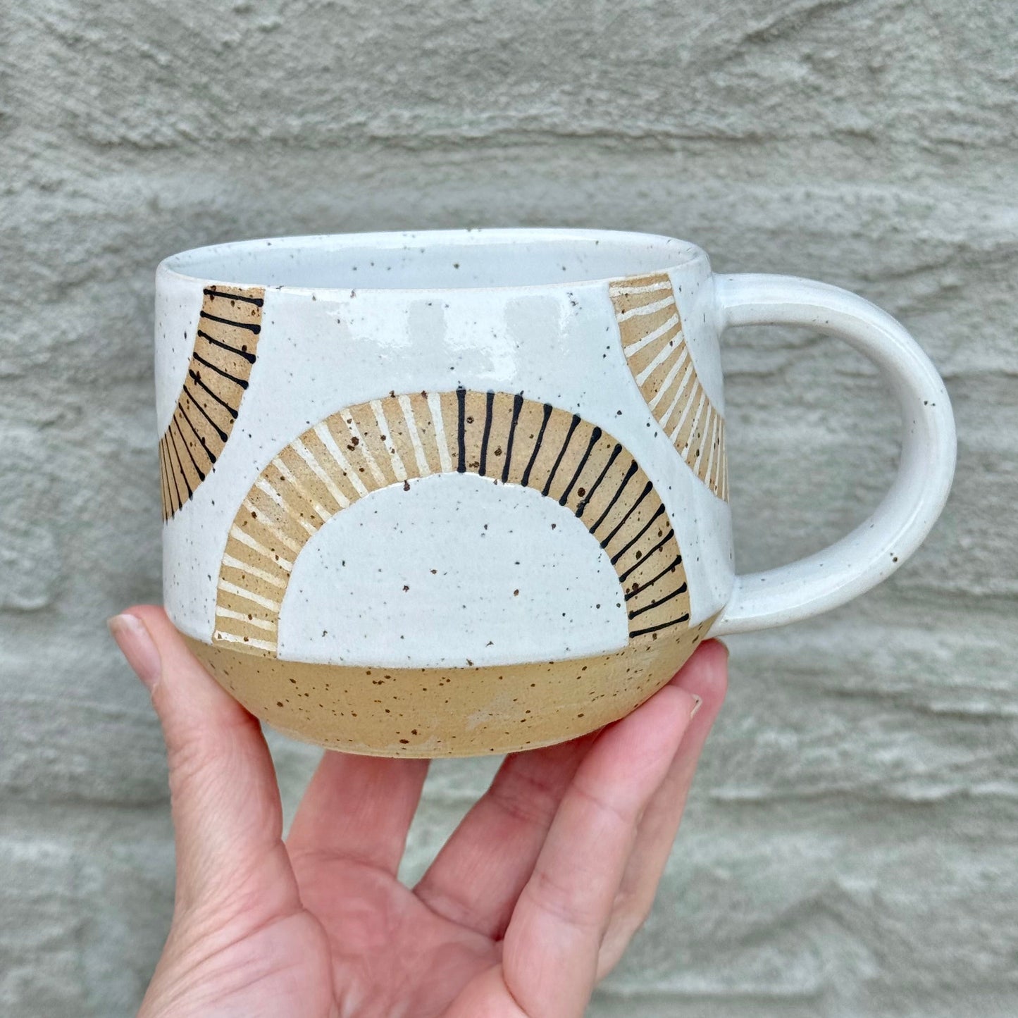 Hand holding a ceramic mug with geometric design against a stone wall background