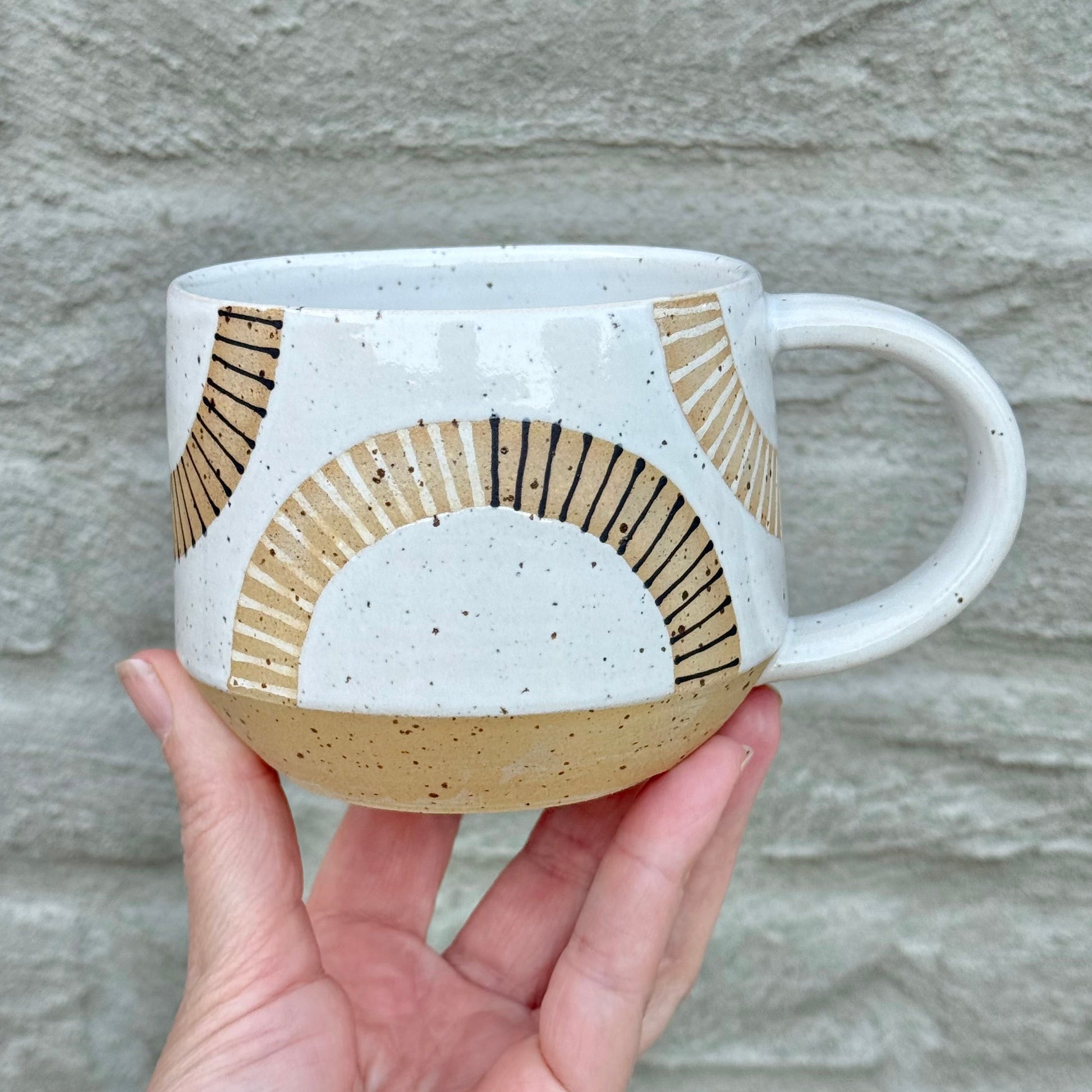 Hand holding a ceramic mug with geometric design against a stone wall background