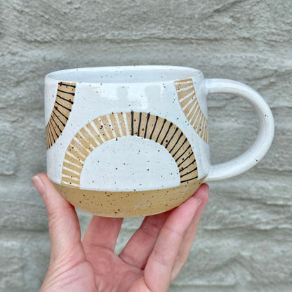 Hand holding a ceramic mug with geometric design against a stone wall background