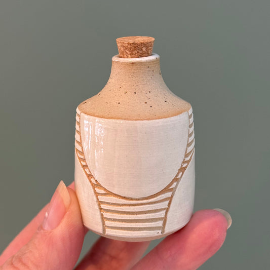 Hand holding a small ceramic bottle with decorative patterns against a plain background