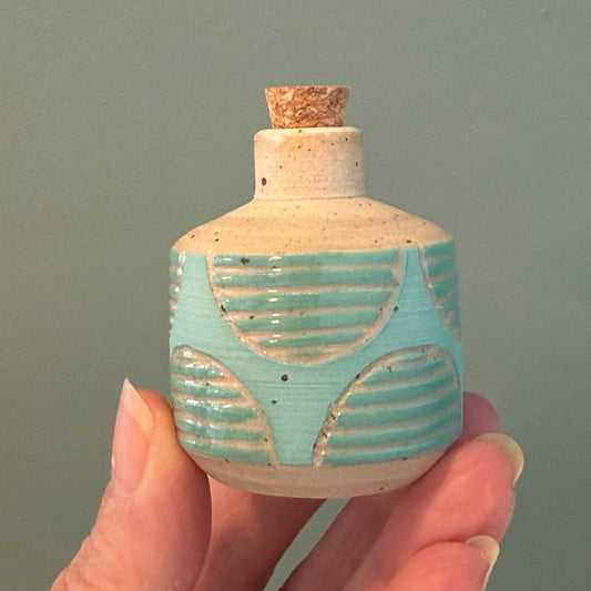 Hand holding a small ceramic bottle with a decorative pattern against a plain background