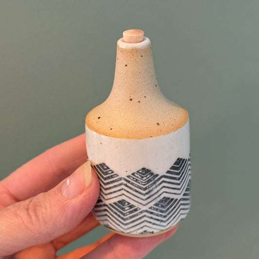 Ceramic bottle with geometric pattern held in a hand against a neutral background