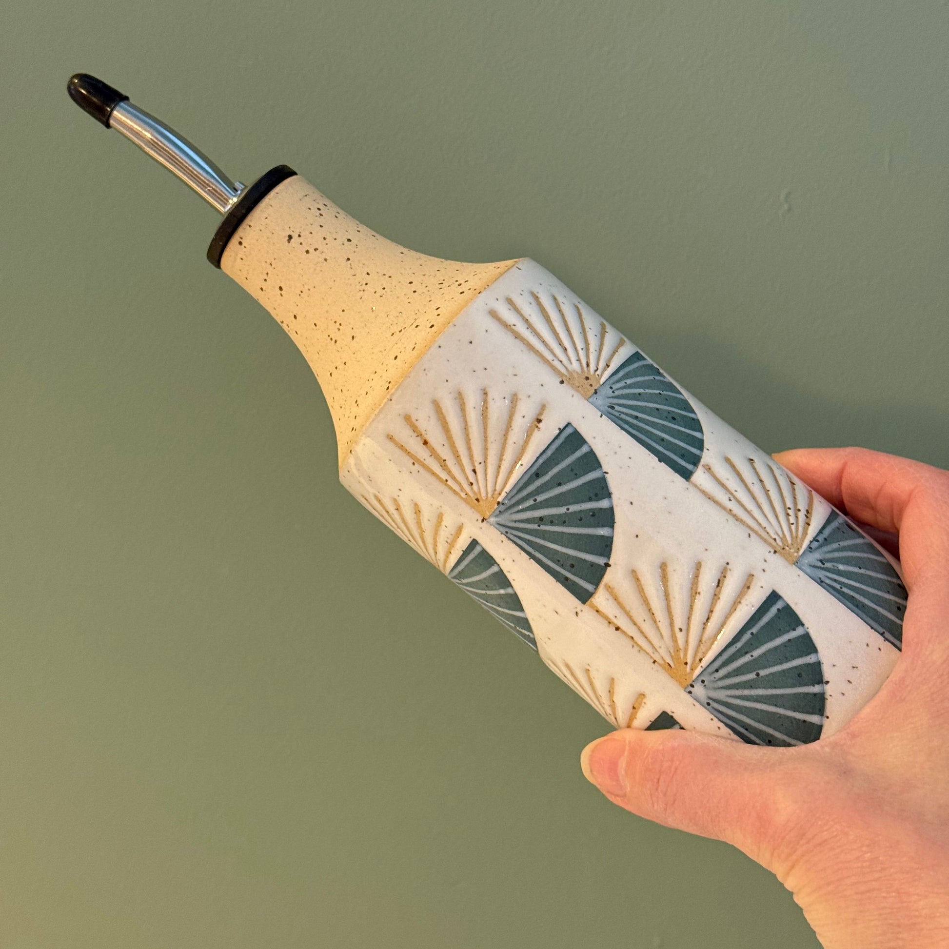 Hand holding a ceramic oil bottle with decorative surface against a plain background