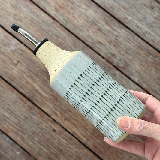 Hand holding an oil bottle, decorated in a teardrop pattern in green and grey on a wooden background