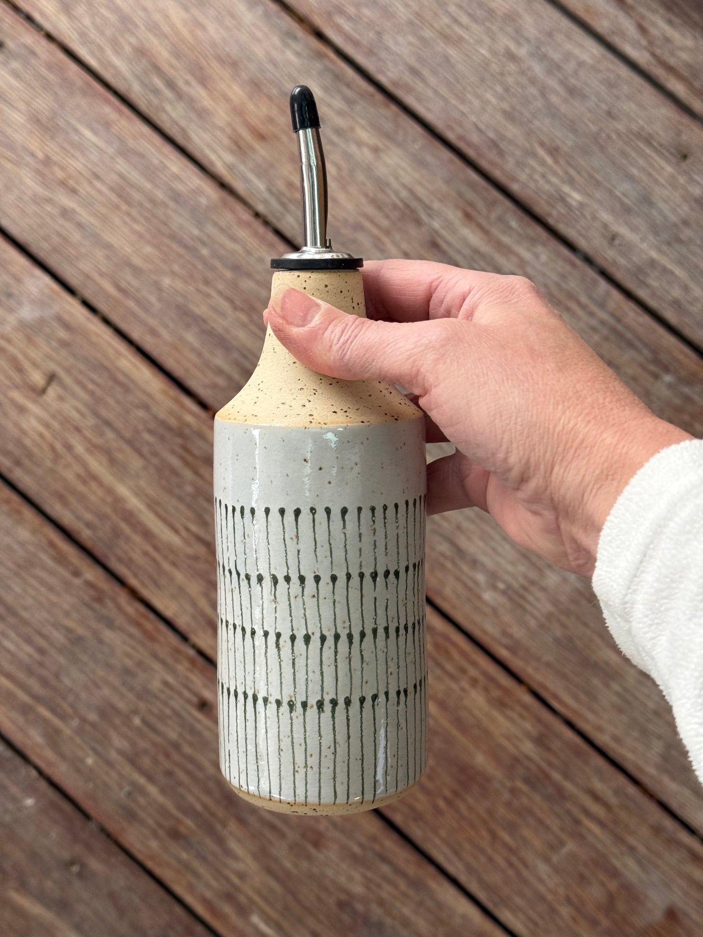 Hand holding an oil bottle with a teardrop design on a wooden surface